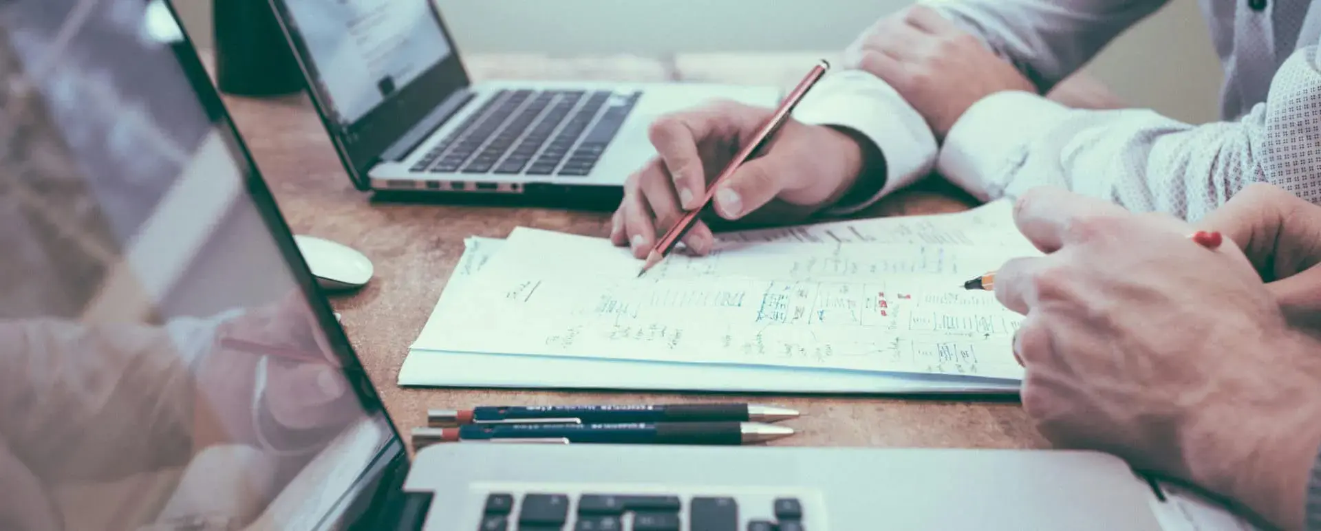 Two people reviewing handwritten financial notes and laptops at a desk