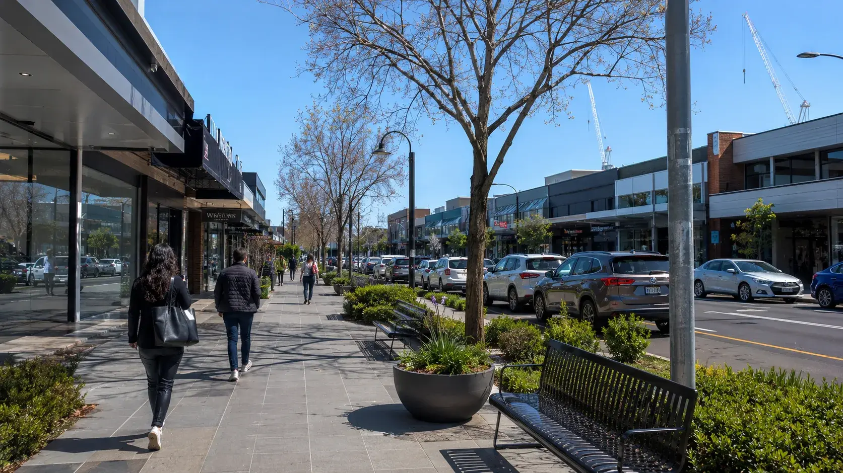 Pedestrians walking along a Doncaster shopping strip with shopfronts, parked cars and street trees