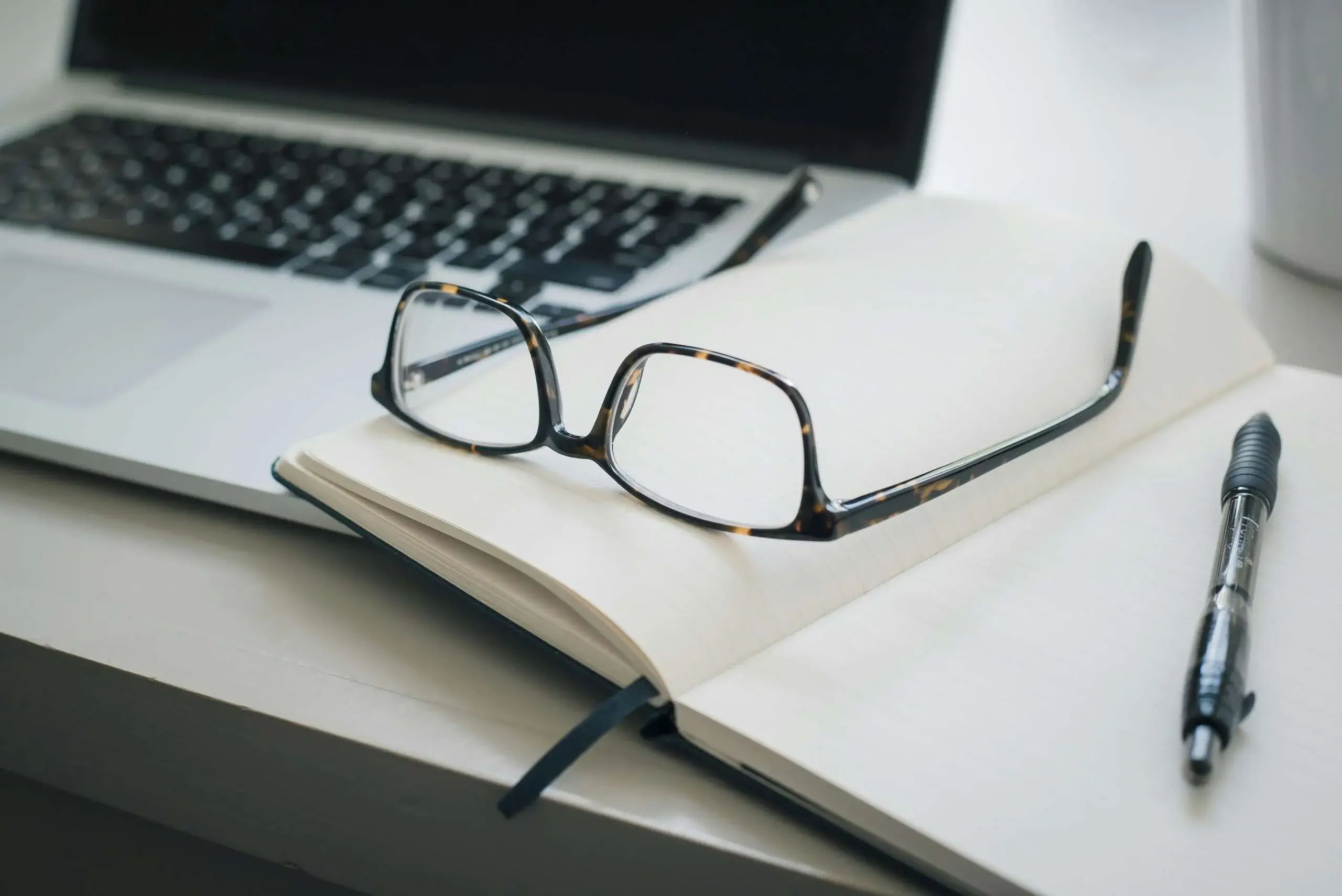 Glasses resting on an open notebook next to a laptop