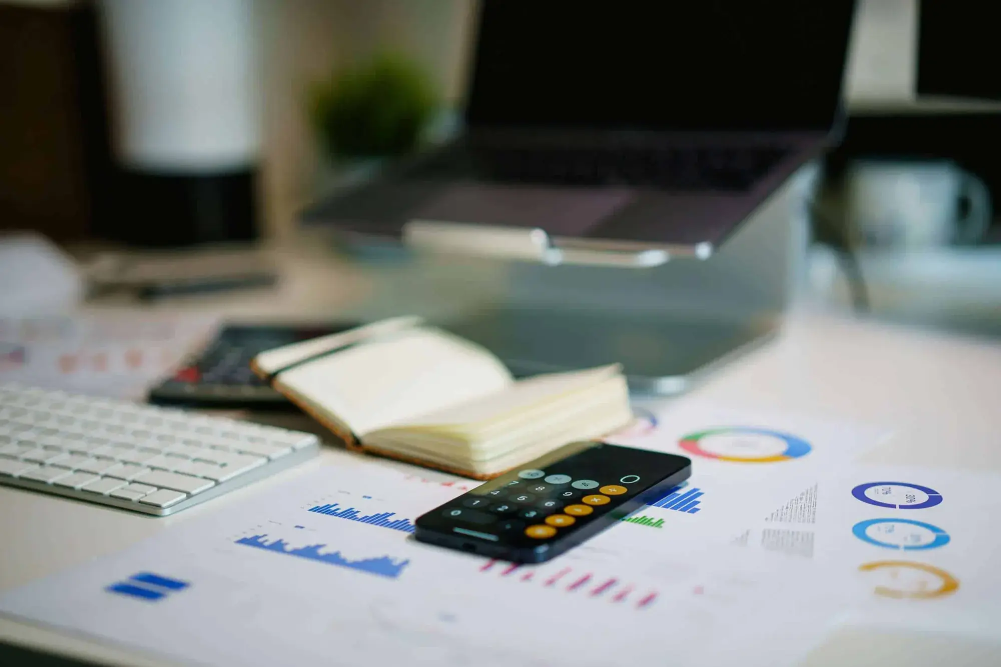 Calculator, printed financial charts and an open notebook on a desk beside a laptop, representing a business working out its taxable income