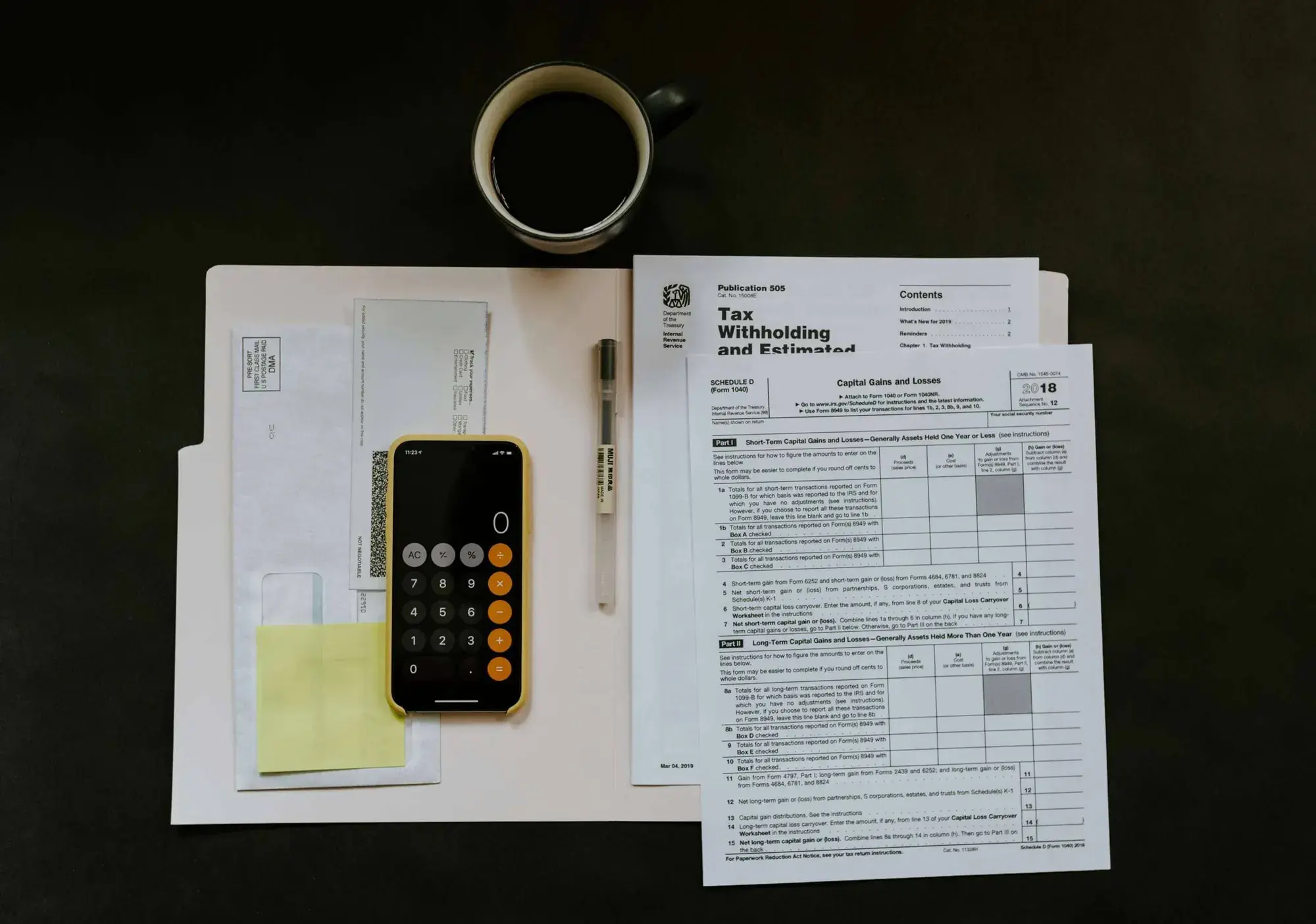 A phone calculator resting on printed tax forms and schedules next to a coffee cup on a desk, representing the paperwork bookkeepers and accountants both work with
