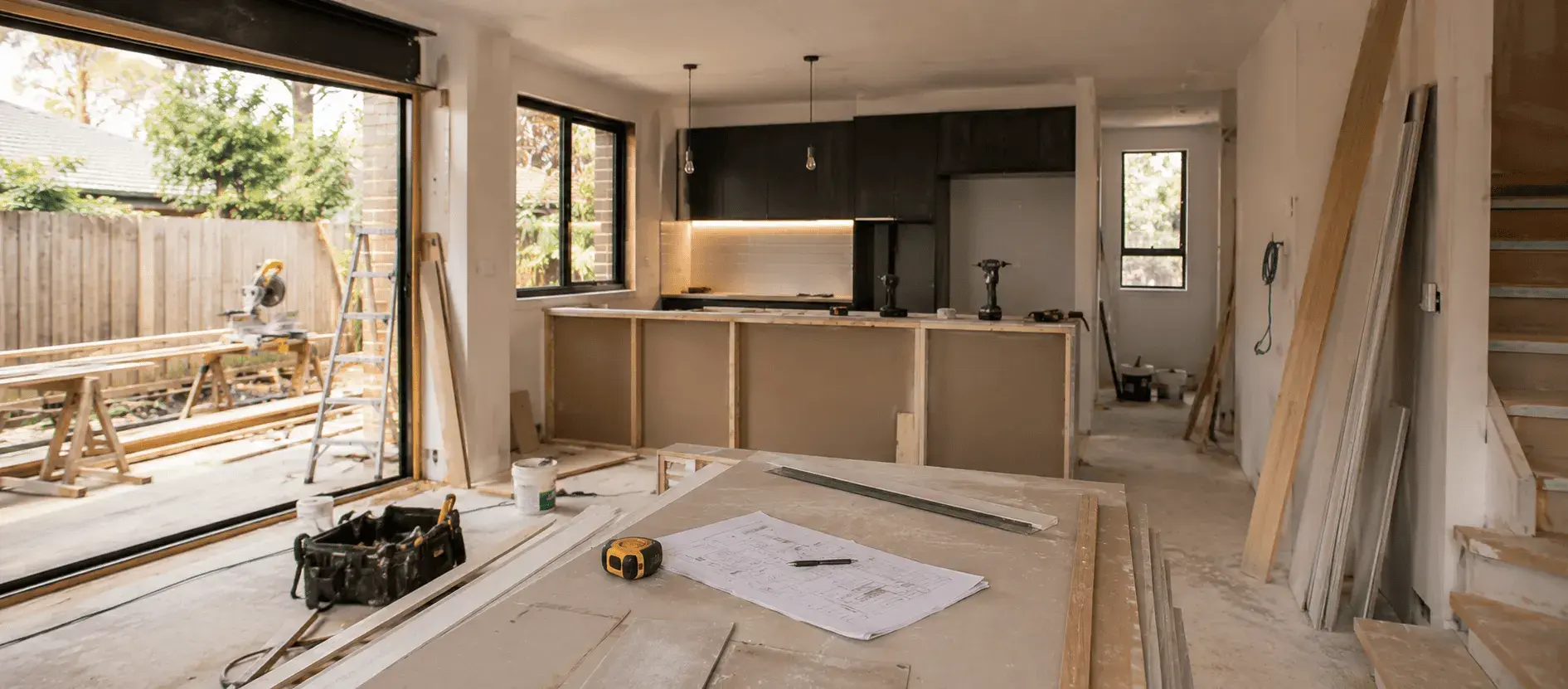 Interior of a house mid-renovation with power tools, timber offcuts and building plans laid out on a makeshift workbench